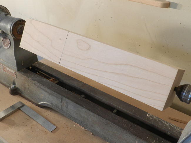 photo of 4 x 4 coffee table leg mounted between lathe centers with scribe mark to indicate turned cylindrical section